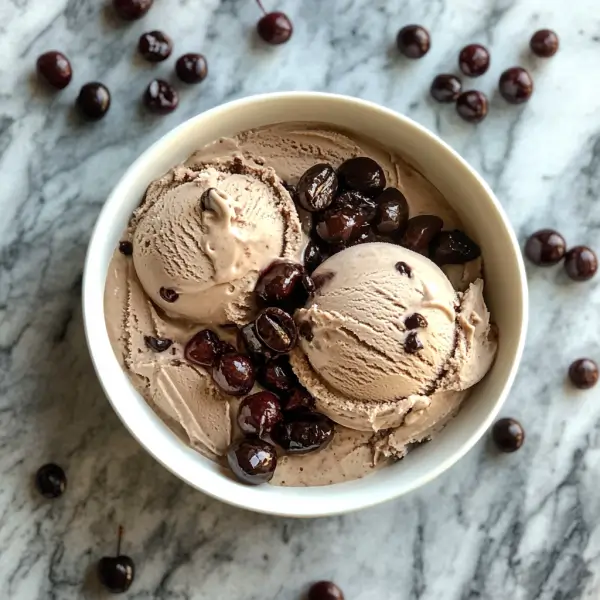 A scoop of homemade black cherry coffee ice cream, rich and creamy, served in a bowl with fresh black cherries and a drizzle of coffee on the side.